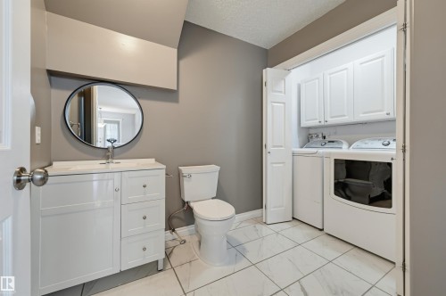 White vanity with a single basin, circular mirror, white toilet, and tile flooring - #8 1920 Millwoods Rd E Nw, Edmonton, AB - Indoor Photo Showing Laundry Room