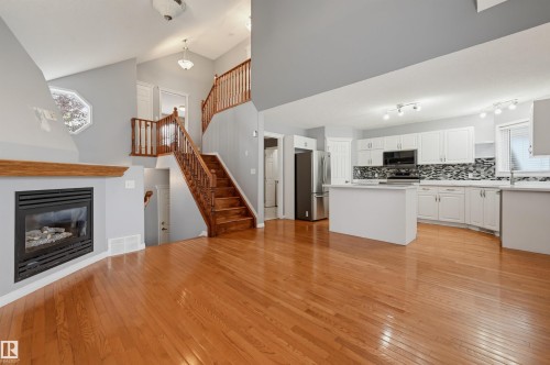 Open-concept living area with wood-finish flooring, a built-in fireplace, and a light wood staircase - #8 1920 Millwoods Rd E Nw, Edmonton, AB - Indoor Photo Showing Kitchen With Fireplace