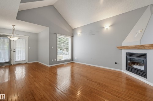 Vaulted ceilings, wood-finish flooring, a built-in fireplace with a wood mantle, transom windows, and a hanging light fixture - #8 1920 Millwoods Rd E Nw, Edmonton, AB - Indoor With Fireplace