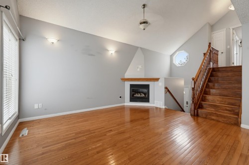 Vaulted ceiling, hardwood flooring, built-in fireplace with wood mantel, hardwood staircase with wood railing, and an octagonal window - #8 1920 Millwoods Rd E Nw, Edmonton, AB - Indoor With Fireplace