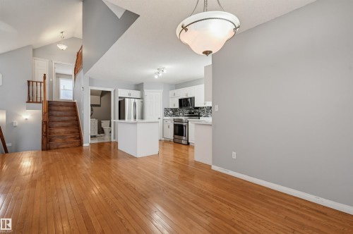 Hardwood flooring throughout, white kitchen cabinetry, stainless steel appliances, kitchen island, and a decorative tile backsplash - #8 1920 Millwoods Rd E Nw, Edmonton, AB - Indoor Photo Showing Kitchen
