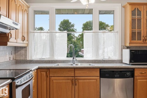 Double basin stainless steel sink with a high-arc faucet, wood cabinetry, stone-finish countertops, tile backsplash, and a black and stainless steel dishwasher - 7 Graham Avenue, St. Albert, AB - Indoor Photo Showing Kitchen With Double Sink