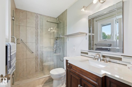 Vanity with an integrated sink and brushed nickel faucet, glass mosaic tile backsplash, framed mirror with track lighting, and a walk-in shower with tile surround and glass enclosure - 7 Graham Avenue, St. Albert, AB - Indoor Photo Showing Bathroom