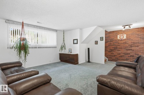 Accent brick wall, window with vertical blinds, light-colored carpeting, recessed lighting, and wall-mounted track lighting - 7 Graham Avenue, St. Albert, AB - Indoor Photo Showing Living Room