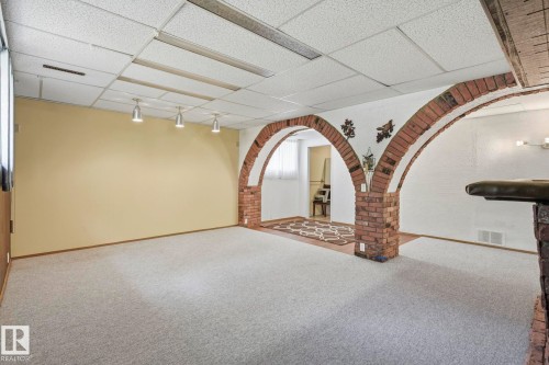 Spacious finished basement featuring exposed brick archways, neutral carpet flooring, recessed lighting, and yellow accent walls - 7 Graham Avenue, St. Albert, AB - Indoor Photo Showing Other Room