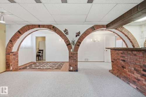 Two brick archways, a brick-clad bar, light-toned carpeting, and a drop ceiling with recessed lighting - 7 Graham Avenue, St. Albert, AB - Indoor Photo Showing Other Room