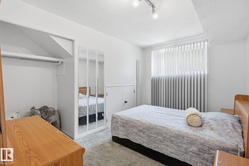 Recessed closet with clothes rod, mirrored wardrobe doors, window with vertical blinds, track lighting, and wood-finish headboard - 7 Graham Avenue, St. Albert, AB - Indoor Photo Showing Bedroom