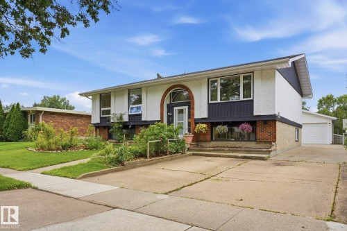 Exterior featuring white stucco and dark siding, brick accents, arched entry door, and an attached garage with a concrete driveway - 7 Graham Avenue, St. Albert, AB - Outdoor