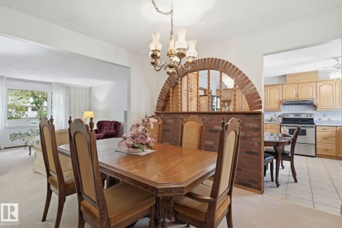 Dining area featuring a decorative brick archway, a chandelier, and an open layout to a kitchen with wood-finish cabinetry and tiled flooring - 7 Graham Avenue, St. Albert, AB - Indoor Photo Showing Dining Room
