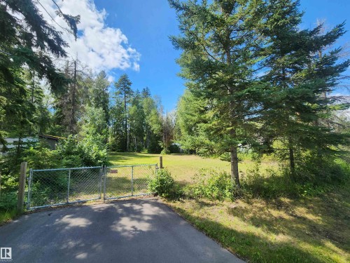 Paved driveway with a chain-link gate, leading to an expansive grassy area - #413 55230 Rge Road 10, Rural Sturgeon County, AB 