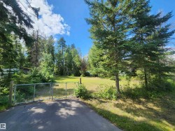 Paved driveway with a chain-link gate, leading to an expansive grassy area - 