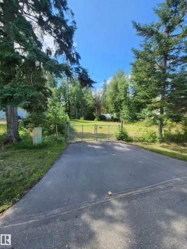 Paved driveway with a chain-link gate, surrounded by mature evergreen trees and natural landscaping - #413 55230 Rge Road 10, Rural Sturgeon County, AB 