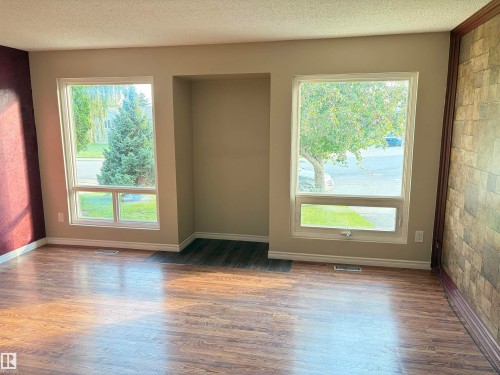 Wood-finish flooring, two large windows, built-in alcove, textured accent wall, and stone-look accent wall - 13831 23 Street Nw, Edmonton, AB - Indoor Photo Showing Other Room