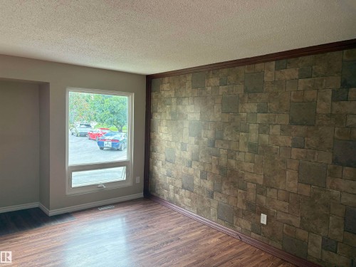 Wood-finish flooring, accent wall with stone-look paneling, white trim, and a prominent window - 13831 23 Street Nw, Edmonton, AB - Indoor Photo Showing Other Room