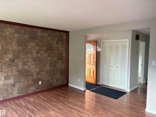 Wood-finish flooring, accent wall with stone-look paneling, and a solid wood entry door with an arched transom window - 13831 23 Street Nw, Edmonton, AB - Indoor Photo Showing Other Room