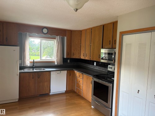 Oak cabinetry with black hardware, stainless steel appliances, dual basin sink, wood-finish flooring, and a double-panel closet with louvered doors - 13831 23 Street Nw, Edmonton, AB - Indoor Photo Showing Kitchen With Double Sink