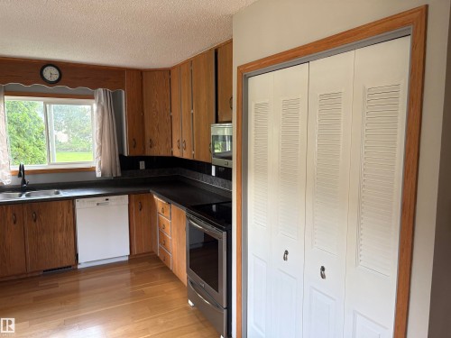 Kitchen featuring wood-finish cabinetry, dark countertops, a stainless steel oven, and a white dishwasher - 13831 23 Street Nw, Edmonton, AB - Indoor Photo Showing Kitchen With Double Sink