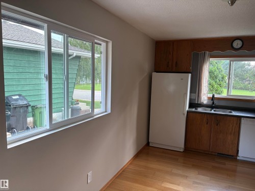 Wood-finish flooring, white double-pane sliding windows, wood cabinetry, and a double basin sink with a black faucet - 13831 23 Street Nw, Edmonton, AB - Indoor Photo Showing Kitchen With Double Sink