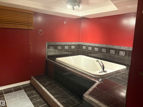 Built-in soaking tub with deck-mounted faucet, surrounded by dark-toned tile - 13831 23 Street Nw, Edmonton, AB - Indoor Photo Showing Laundry Room