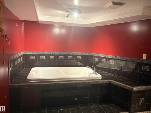 Built-in soaking tub surrounded by dark tile, featuring a decorative border and a red accent wall - 13831 23 Street Nw, Edmonton, AB - Indoor Photo Showing Laundry Room