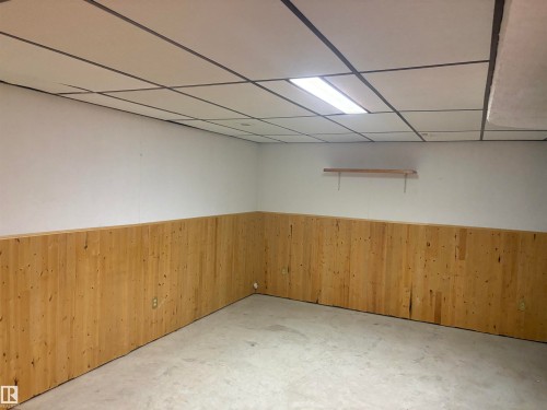 Wood paneling on lower walls, concrete flooring, and drop ceiling with integrated lighting - 13831 23 Street Nw, Edmonton, AB - Indoor
