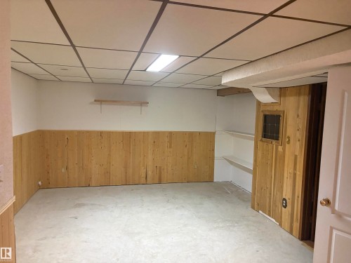 Room featuring light wood paneling, built-in shelving, concrete flooring, and a drop ceiling with integrated lighting - 13831 23 Street Nw, Edmonton, AB - Indoor