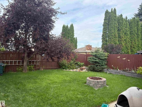 Expansive backyard featuring a manicured lawn, established trees, a stone-finish fire pit, and a tall privacy fence - 13831 23 Street Nw, Edmonton, AB - Outdoor