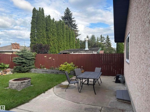 Expansive backyard featuring a concrete patio, a built-in stone fire pit, a perimeter fence, and mature landscaping - 13831 23 Street Nw, Edmonton, AB - Outdoor