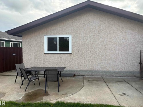 Stucco exterior with a brown roofline, featuring a white-framed sliding window and a concrete patio - 13831 23 Street Nw, Edmonton, AB - Outdoor