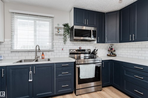 Kitchen featuring blue shaker-style cabinetry, stainless steel appliances, a subway tile backsplash, and light-toned countertops - 4521 29 Avenue Nw, Edmonton, AB - Indoor Photo Showing Kitchen With Double Sink With Upgraded Kitchen