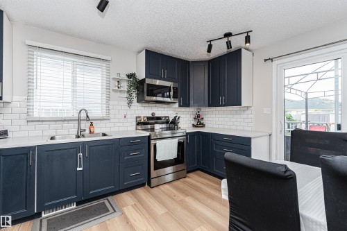 Navy blue shaker-style cabinetry, stainless steel appliances, subway tile backsplash, light wood-finish flooring, and track lighting - 4521 29 Avenue Nw, Edmonton, AB - Indoor Photo Showing Kitchen With Double Sink With Upgraded Kitchen