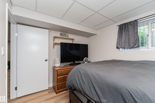 Wood-finish flooring with a white door, drop ceiling, and a single window with security bars - 4521 29 Avenue Nw, Edmonton, AB - Indoor Photo Showing Bedroom
