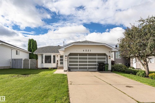 Single-story residence featuring white siding, an attached garage with a modern glass panel door, a concrete driveway, and a front lawn with mature trees - 4521 29 Avenue Nw, Edmonton, AB - Outdoor With Facade