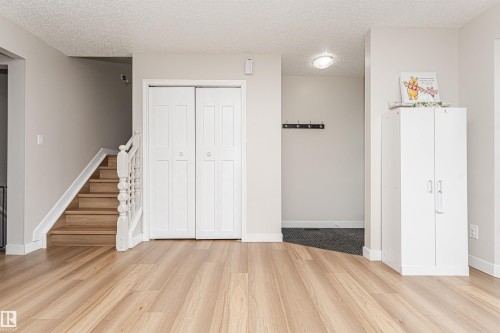 Wood-finish flooring throughout, white bi-fold doors, wood staircase with white balusters, overhead flush-mount lighting, and light-toned walls - 4521 29 Avenue Nw, Edmonton, AB - Indoor Photo Showing Other Room