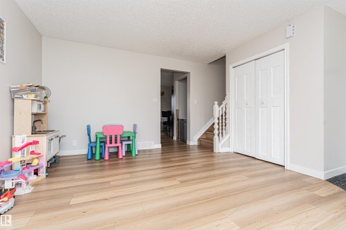 Wood-finish flooring, light gray wall tones, white baseboards, bi-fold closet doors, and a wood staircase with white balusters - 4521 29 Avenue Nw, Edmonton, AB - Indoor Photo Showing Other Room