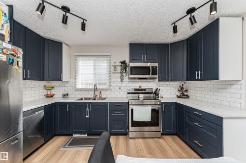 Kitchen featuring dark blue cabinetry, white subway tile backsplash, white countertops, stainless steel appliances, and wood-finish flooring - 4521 29 Avenue Nw, Edmonton, AB - Indoor Photo Showing Kitchen With Double Sink With Upgraded Kitchen