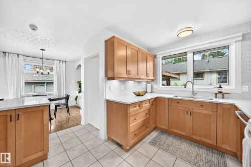 Light wood-finish cabinetry with dark hardware, L-shaped countertop, undermount sink with gooseneck faucet, light tile backsplash, and light tile flooring - 16406 87A Avenue Nw, Edmonton, AB - Indoor Photo Showing Kitchen