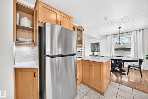 Stainless steel refrigerator, white subway tile backsplash, light wood cabinetry, white countertops, and wood-finish flooring - 16406 87A Avenue Nw, Edmonton, AB - Indoor Photo Showing Other Room