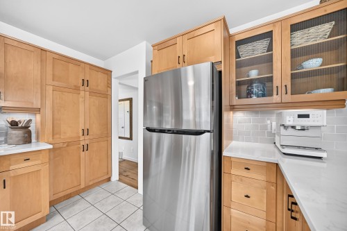Stainless steel refrigerator, light wood-finish cabinetry, light-toned countertops, subway tile backsplash, and ceramic tile flooring - 16406 87A Avenue Nw, Edmonton, AB - Indoor Photo Showing Kitchen