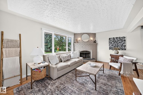 Recessed corner fireplace with a light brick surround, hardwood flooring, and large windows - 16406 87A Avenue Nw, Edmonton, AB - Indoor Photo Showing Living Room With Fireplace