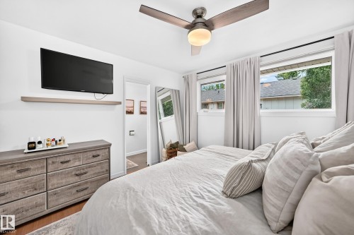 Wood-finish flooring, ceiling fan with integrated lighting, wall-mounted television, and a floating shelf - 16406 87A Avenue Nw, Edmonton, AB - Indoor Photo Showing Bedroom