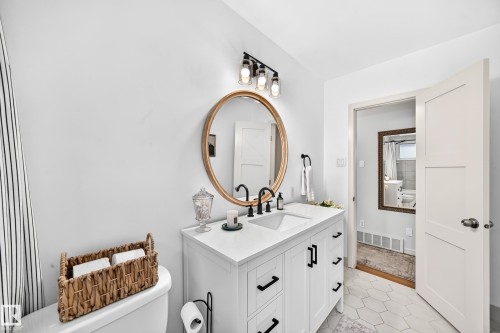 White vanity with dual integrated sinks, matte black hardware, and a gold-framed round mirror - 16406 87A Avenue Nw, Edmonton, AB - Indoor Photo Showing Bathroom