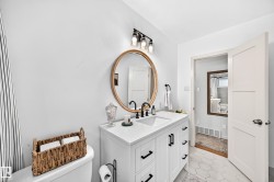 White vanity with dual integrated sinks, matte black hardware, and a gold-framed round mirror - 