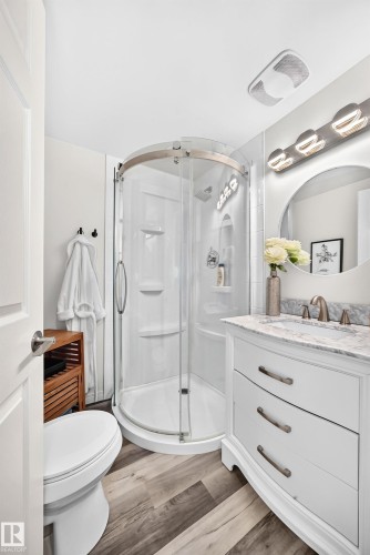 Curved glass shower enclosure, single vanity with integrated sink, stone countertop, wood-finish flooring, and wall-mounted vanity lighting - 16406 87A Avenue Nw, Edmonton, AB - Indoor Photo Showing Bathroom