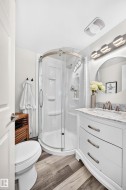 Curved glass shower enclosure, single vanity with integrated sink, stone countertop, wood-finish flooring, and wall-mounted vanity lighting - 