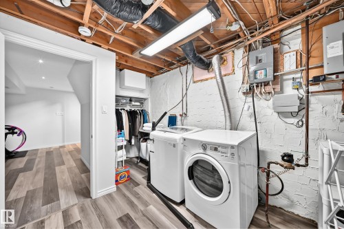 Laundry area with wood-finish flooring, exposed ceiling joists, and white painted brick walls - 16406 87A Avenue Nw, Edmonton, AB - Indoor Photo Showing Laundry Room