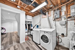 Laundry area with wood-finish flooring, exposed ceiling joists, and white painted brick walls - 