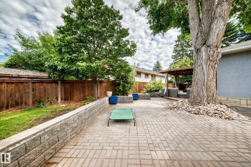 Spacious paver patio with a wood privacy fence, stone retaining wall, mature trees, and a covered outdoor seating area - 16406 87A Avenue Nw, Edmonton, AB - Outdoor