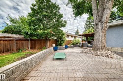Spacious paver patio with a wood privacy fence, stone retaining wall, mature trees, and a covered outdoor seating area - 