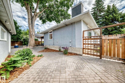 Paver stone driveway with a wooden privacy fence, mature trees, and landscaping elements - 16406 87A Avenue Nw, Edmonton, AB - Outdoor With Exterior